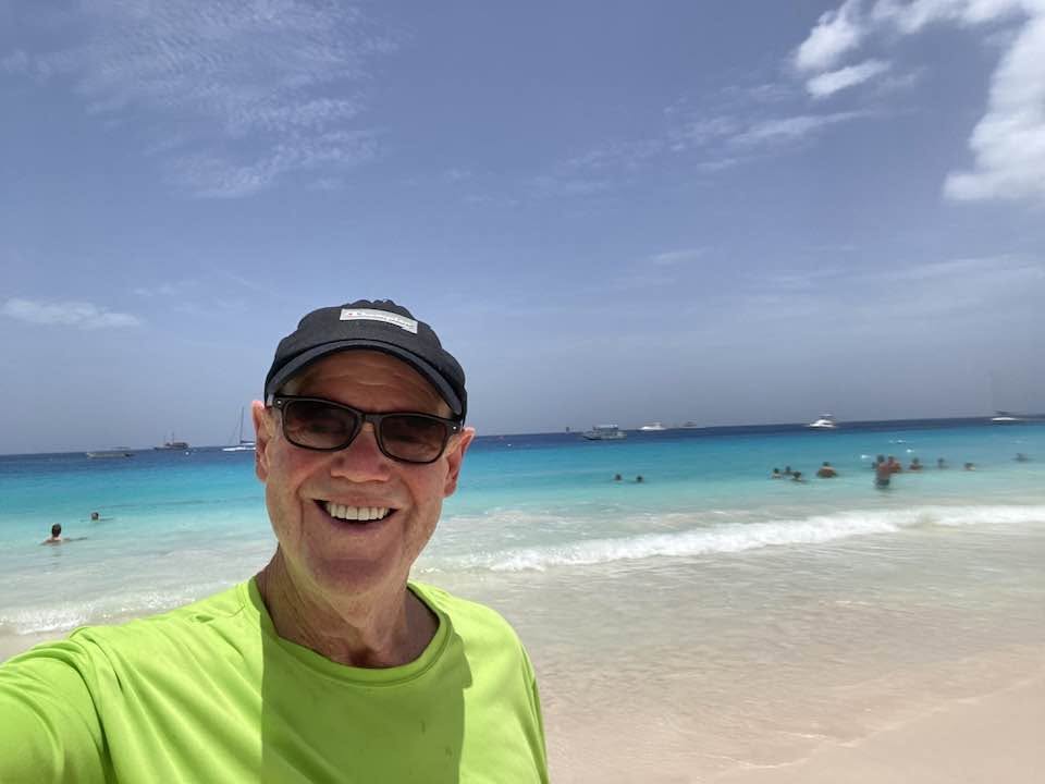 John smiling on the beach in Barbados, turquoise water behind him